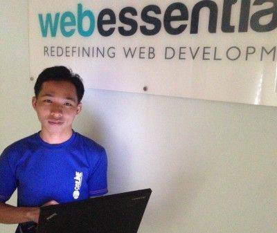 Web Developer Man Math stands in front of the Web Essentials logo, while holding his laptop.